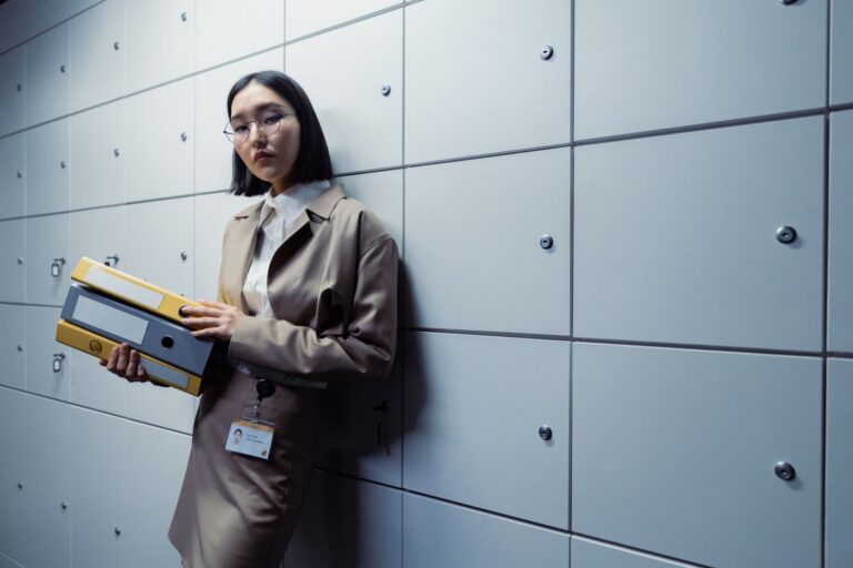 Businesswoman in office attire standing with documents, appearing poised in a modern office setting.