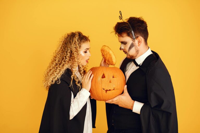 Young couple in costumes holding a carved pumpkin in a studio with yellow background, perfect for Halloween themes.
