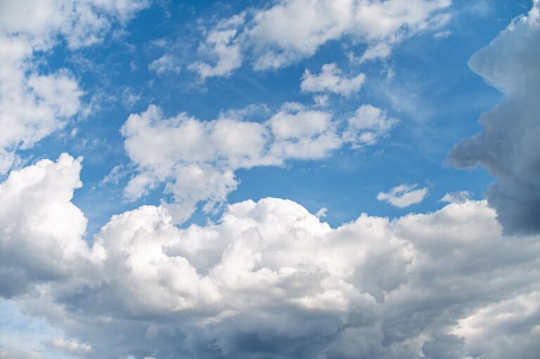 Dramatic cumulus clouds stretch across a vibrant blue sky, creating an awe-inspiring weather scene.