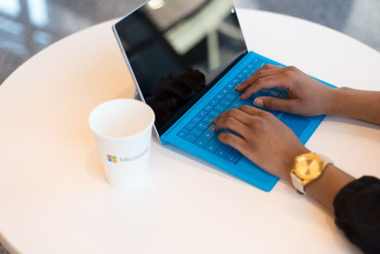 A person working on a laptop with a blue keyboard, using a modern workspace setting.